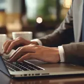 Hands typing on a laptop keyboard, worn by a person in a suit jacket and white shirt.